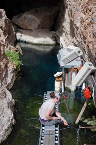 Graduate Student Ambre Chaudoin observes Devils Hole pupfish on a research platform installed above the pool that forms the cave entrance. (Photo by Olin Feuerbacher) Graduate Student Ambre Chaudoin observes Devils Hole pupfish on a research platform installed above the pool that forms the cave entrance. (Photo by Olin Feuerbacher)