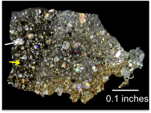 A thin section of the meteorite from this study seen in cross-polarized light. "Viewing it that way can help identify different minerals in the thin section – but it's also prettiest that way," Miller said. "The dark section on the left is the primitive clast we've been studying. The white arrow is pointing to a large silicate chondrule, and the yellow arrow is pointing to a sulfide chondrule, which is black in this view." (Photo courtesy of Kelly Miller) A thin section of the meteorite from this study seen in cross-polarized light. "Viewing it that way can help identify different minerals in the thin section – but it's also prettiest that way," Miller said. "The dark section on the left is the primitive clast we've been studying. The white arrow is pointing to a large silicate chondrule, and the yellow arrow is pointing to a sulfide chondrule, which is black in this view." (Photo courtesy of Kelly Miller)