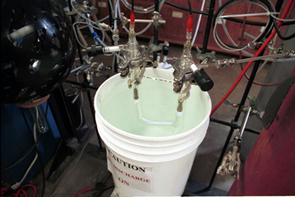 The tholin generator setup in Smith's lab. Chemists use the setup pictured here to make analog tholins tholins by sending high voltage discharges through nitrogen-methane gases under vacuum and low temperatures. Over time, the precipitates collect in the glass tubing immersed in the pail. Scientists collect and analyze these lab-made materials to interpret real Titan data from the Cassini mission and plan a future mission that would deploy an organic chemistry lab to Titan's surface. (Photo: Lori Stiles, UA News) The tholin generator setup in Smith's lab. Chemists use the setup pictured here to make analog tholins tholins by sending high voltage discharges through nitrogen-methane gases under vacuum and low temperatures. Over time, the precipitates collect in the glass tubing immersed in the pail. Scientists collect and analyze these lab-made materials to interpret real Titan data from the Cassini mission and plan a future mission that would deploy an organic chemistry lab to Titan's surface. (Photo: Lori Stiles, UA News)