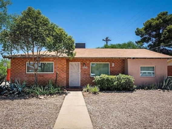 Front view of a single-story brick home with a brown roof and landscaped with shrubs and succulents.