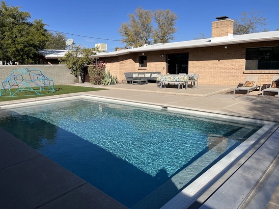 A bright backyard with a shimmering pool, colorful furniture, and a geometric play structure under a clear blue sky.
