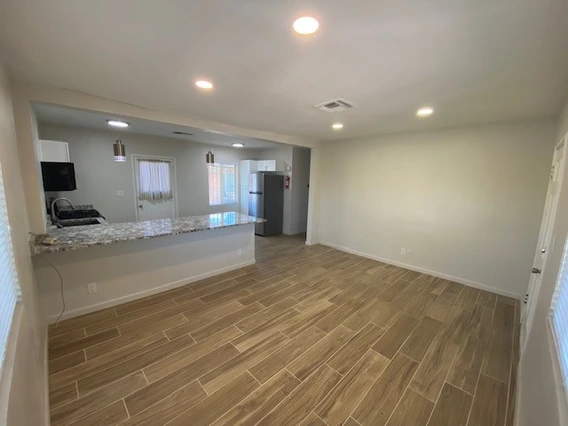 Spacious, modern living area with tiled flooring, a kitchen bar, and natural light from windows, featuring neutral colors throughout.