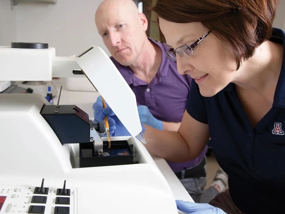 A man and a woman researcher analyze results over a white microscope.