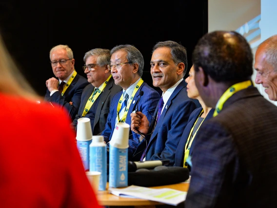 people sitting at a table during a press conference as one of them speaks