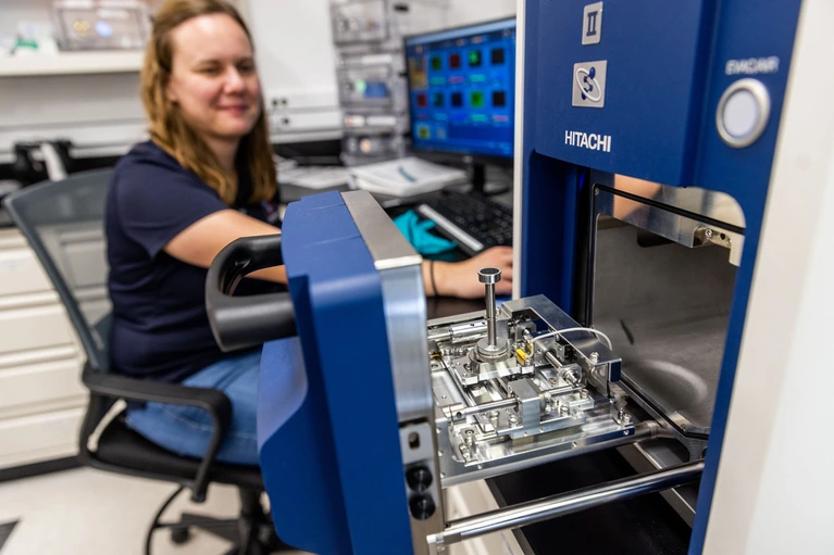 Jessica Barnes sitting in a chair in her lab, loading a sample into an analyzer instrument