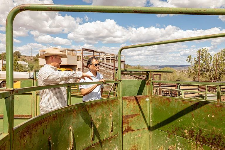 Two men examine agricultural equipment at a ranch.