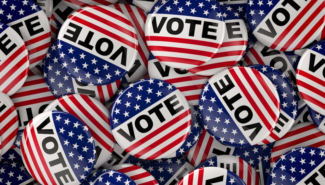 A pile of red, white, and blue "VOTE" buttons featuring stars and stripes, designed to resemble the American flag.