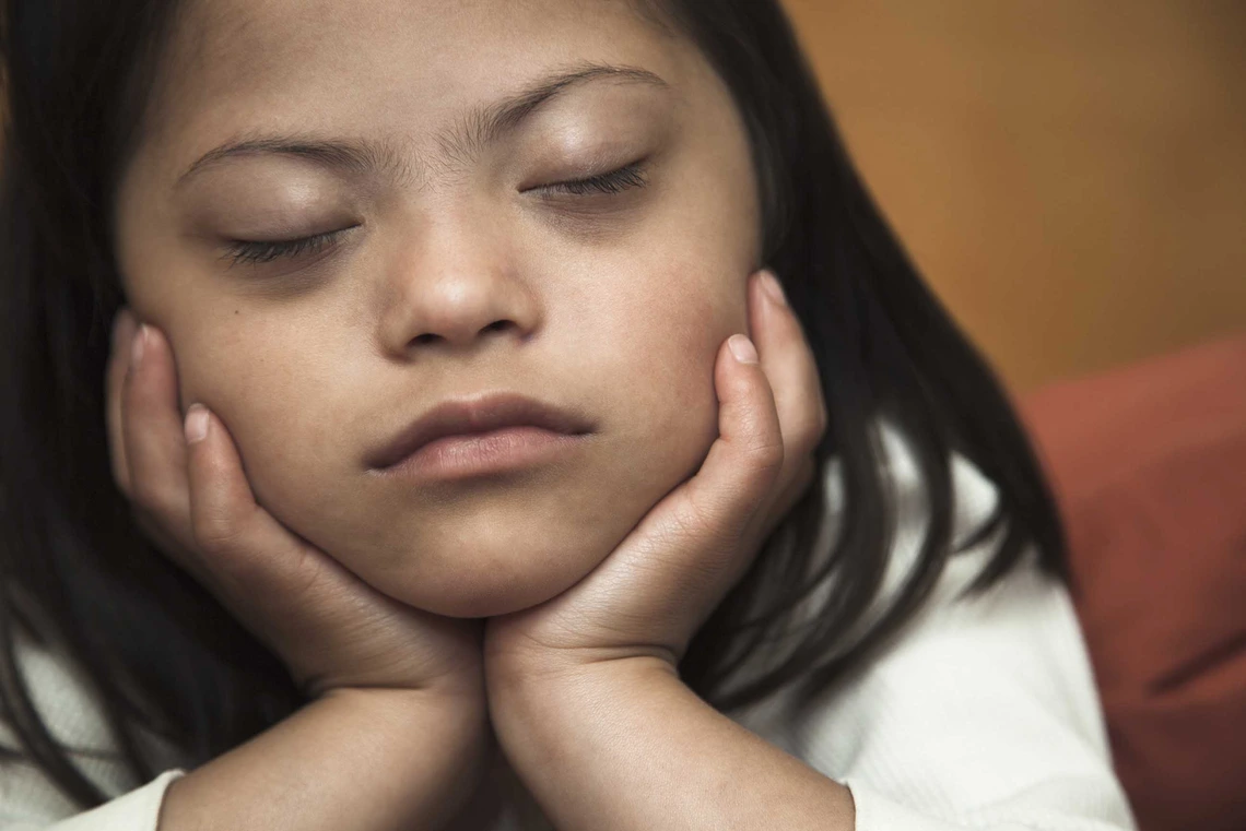 a girl with her eyes closed with her chin resting in her hands