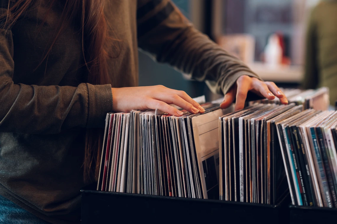 A person flips through a collection of vinyl records in a record store, using both hands to browse the albums in a crate.