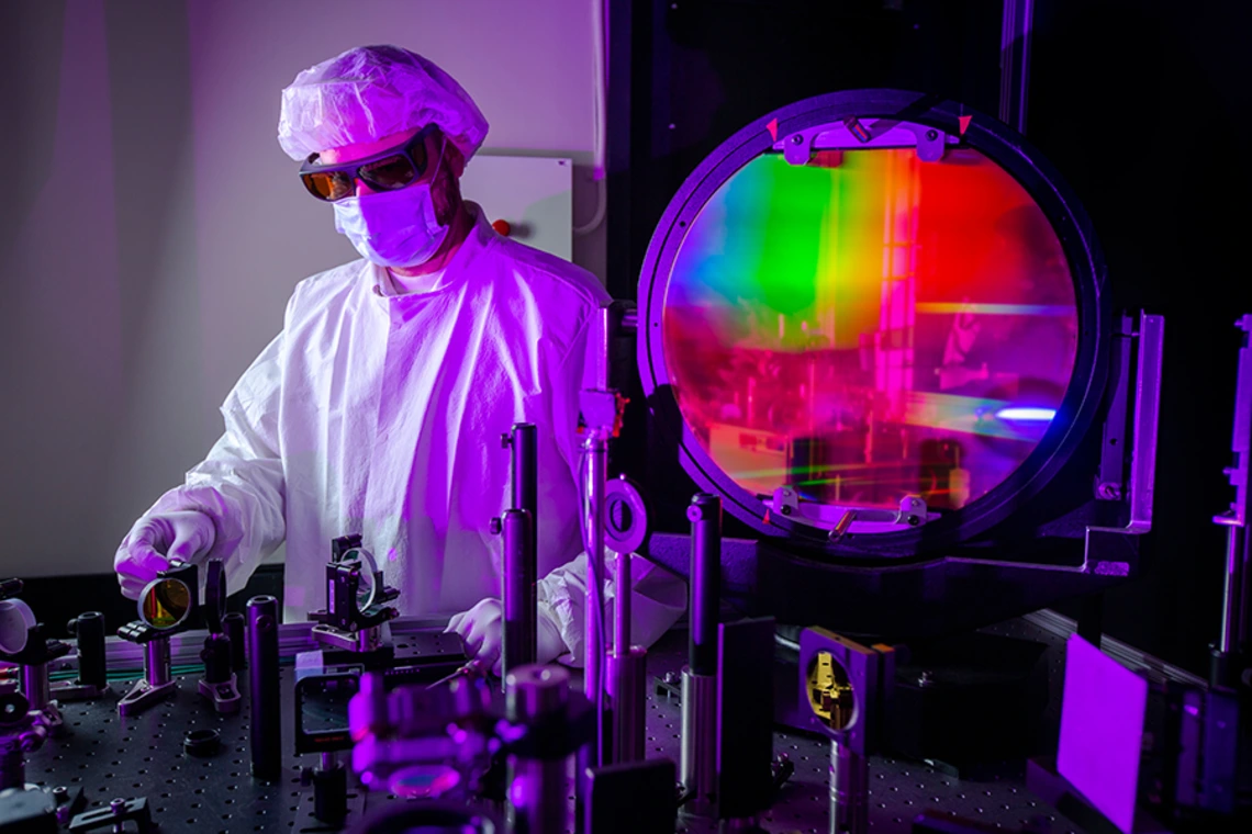 A researcher in a lab coat works on laser technology.