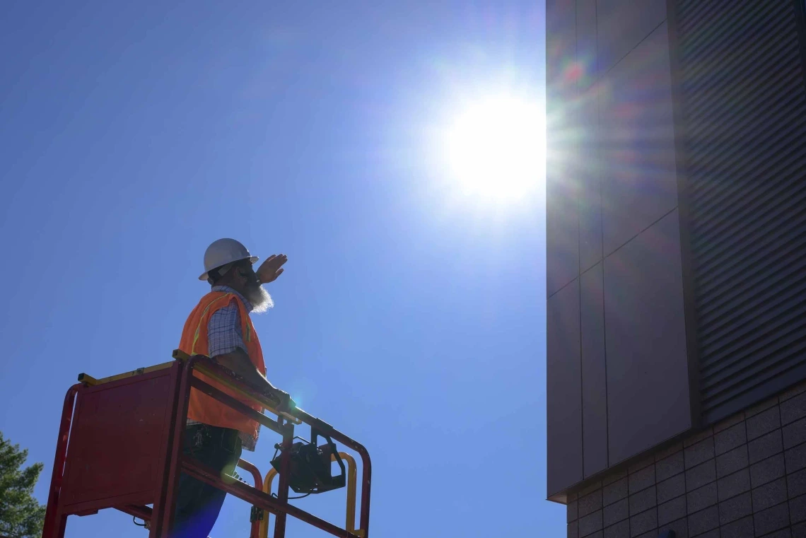 a construction worker standing on a lift near a building in the direct midday sun