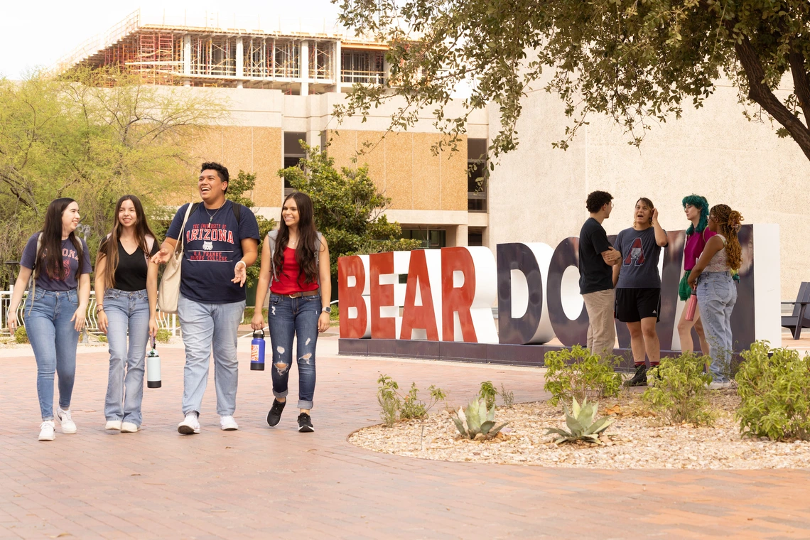 students walking past the U of A main library in front of a large "Bear Down" sign