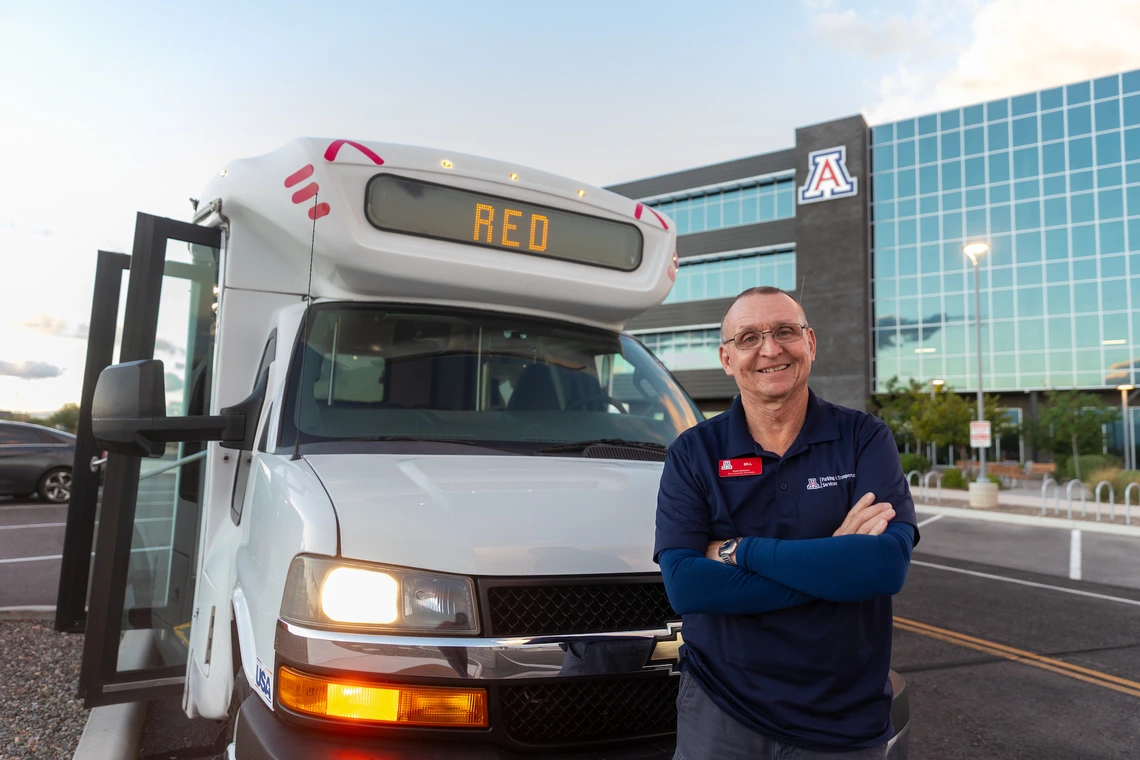 Bill Mason standing outside a Cat Tran shuttle near a building in the background with a Block A logo on it