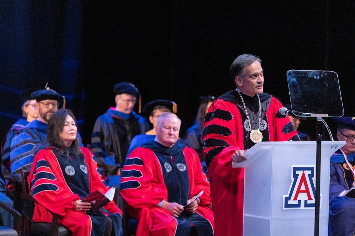 University of Arizona President Suresh Garimella speaks at a podium during the Luminaries Outstanding Faculty Awards ceremony. He wears academic regalia with a red gown and presidential medallion, with faculty members in similar attire seated behind him on stage.
