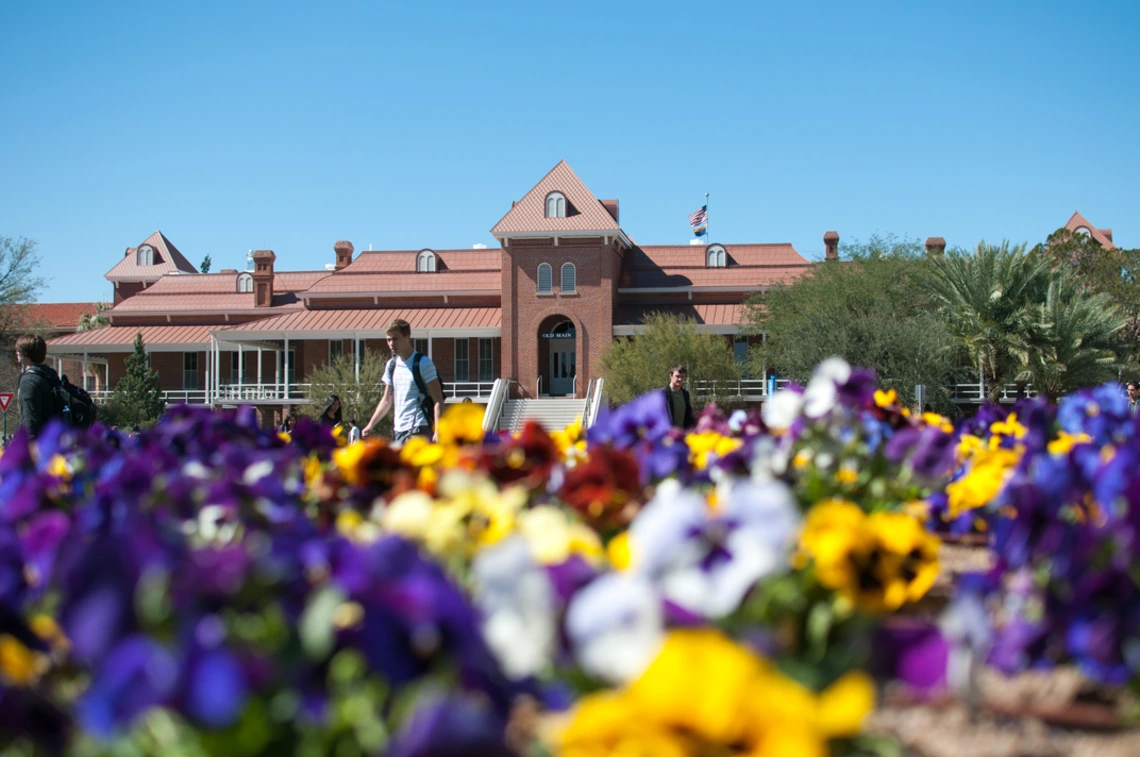 Old Main in the background, with purple, yellow, white and red flowers in the foreground