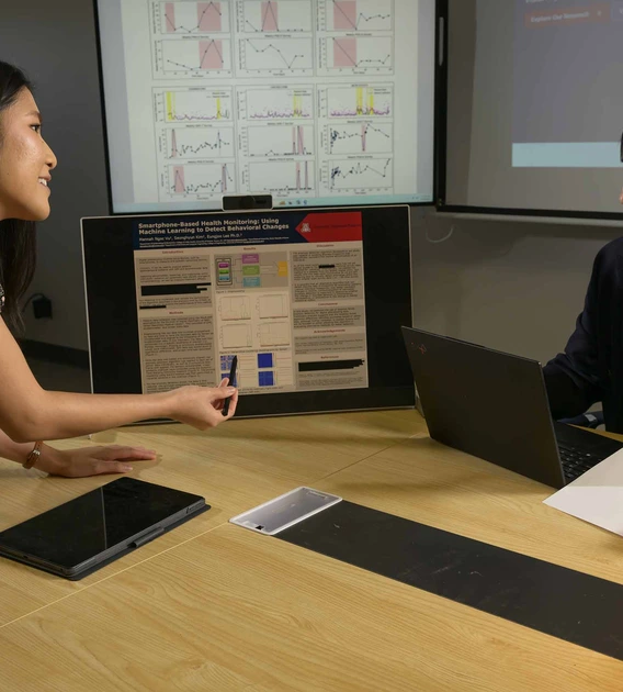 Hannah Vu and Eung-Joo Lee speaking at a conference room table and gesturing toward a screen