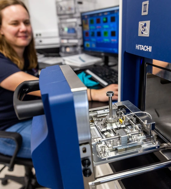 Jessica Barnes sitting in a chair in her lab, loading a sample into an analyzer instrument