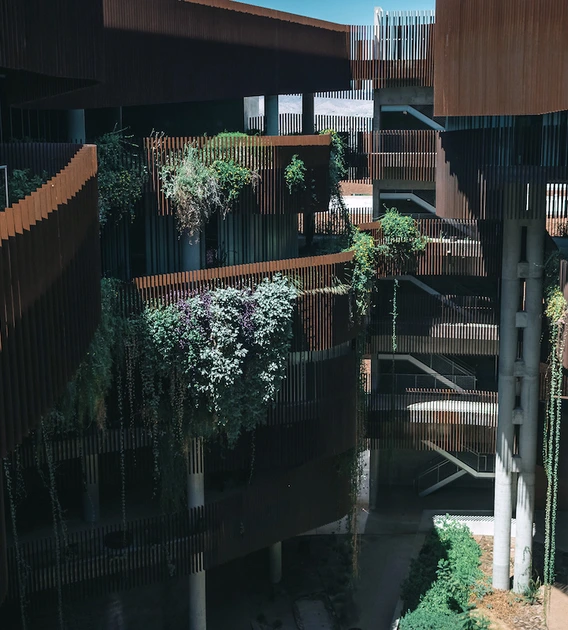Interior view of the ENR2 Building’s canyon-like courtyard, with rust-colored fins, open-air walkways, and terraces covered in hanging vines and greenery.