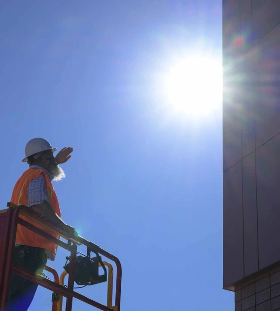 a construction worker standing on a lift near a building in the direct midday sun