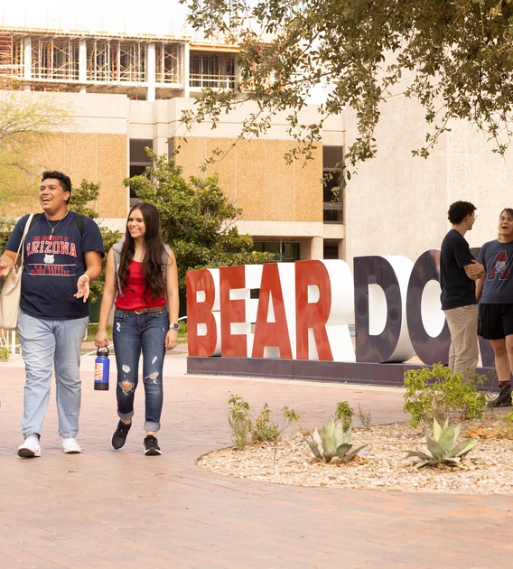 students walking past the U of A main library in front of a large "Bear Down" sign
