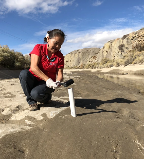 Karletta Chief using a tool to conduct hydrological fieldwork in a riverbed