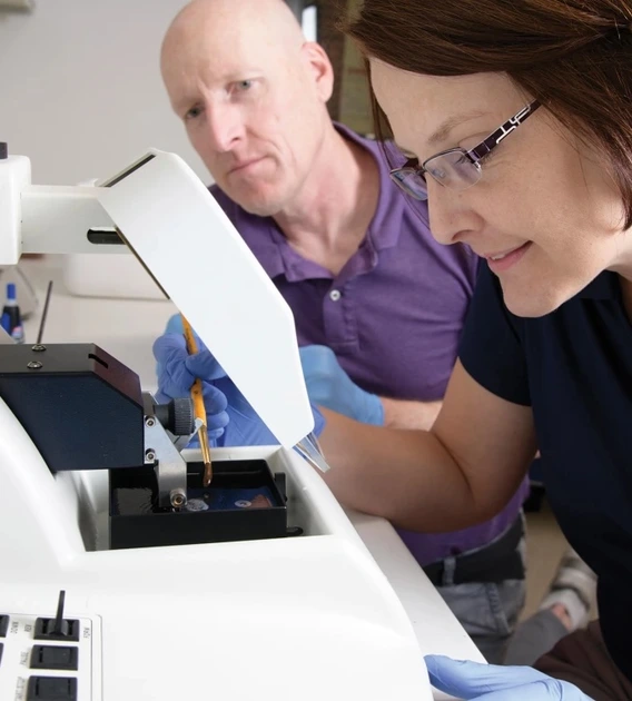 A man and a woman researcher analyze results over a white microscope.