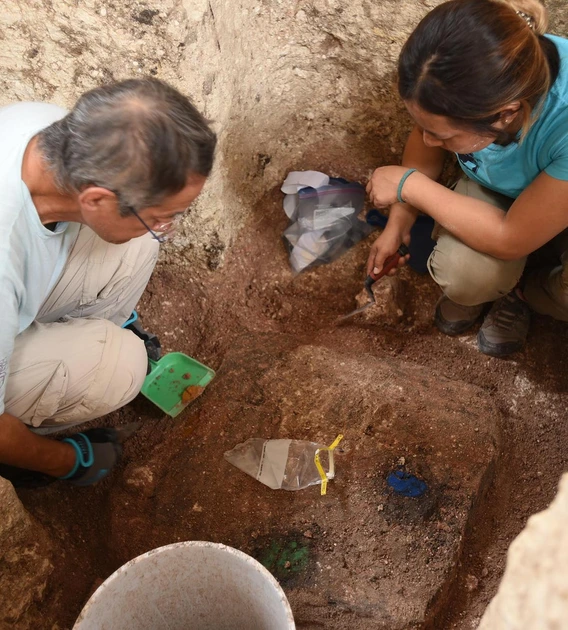 archaeologists crouching in a hole in the ground and digging around artifacts buried in the ground