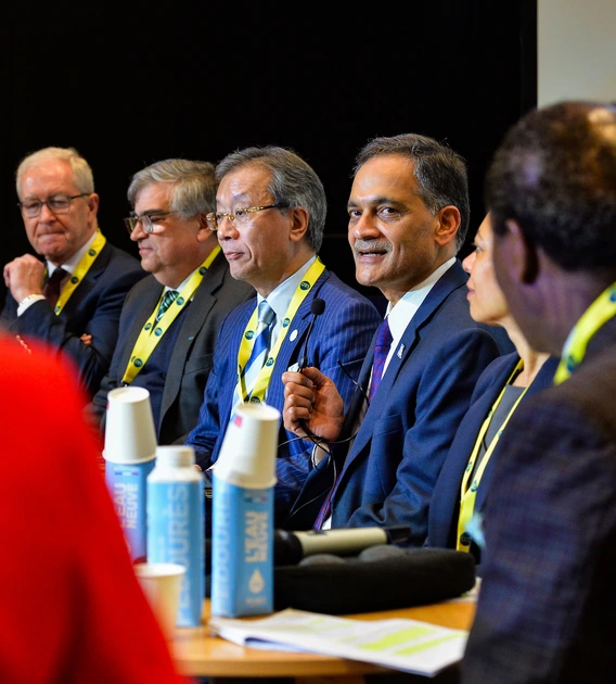 people sitting at a table during a press conference as one of them speaks