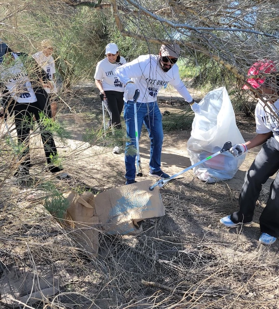 University of Arizona volunteers wearing “Live United” shirts pick up trash and debris in a wooded area using grabbers and large plastic bags during Eller Make a Difference Day.