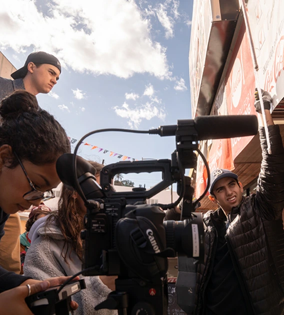 Film students surround a camera and film a scene outside of a restaurant.