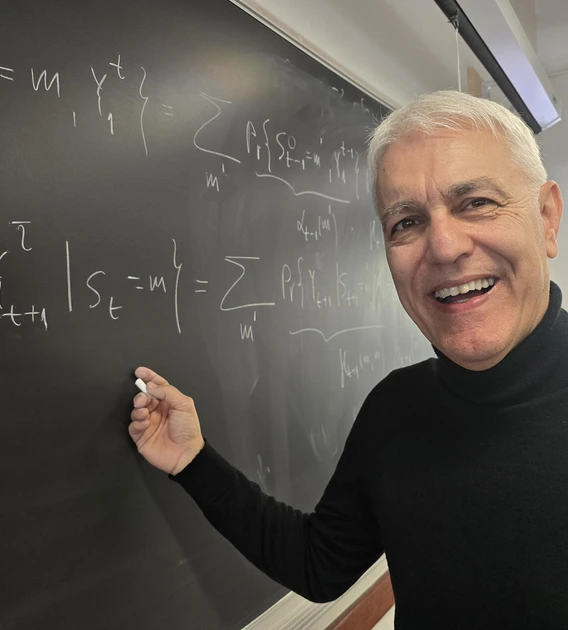 A professor wearing a black shirt writes on a chalkboard