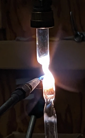 Close-up of a glass vial being heated by a welding torch