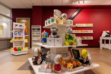 Display of gift items inside the “Gifted” store in the Student Union Memorial Center. The central white shelving unit holds stuffed animals, balloons, mugs, potted plant kits, and small gift baskets. Additional shelves in the background display greeting cards, bottles, and colorful novelty items.