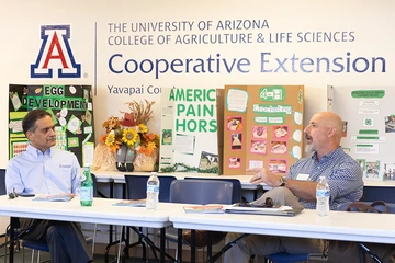 Two men chat in front of poster boards decorated with Cooperative Extension topics.