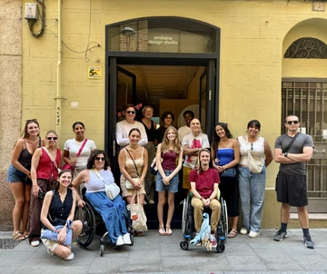 A group of students and instructors smile for a photo outside Emiliana Design Studio in Barcelona, standing and sitting together in front of the entrance.