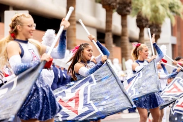 University of Arizona twirlers and flag performers in sparkling blue and white uniforms wave large Wildcat “A” flags during the Homecoming parade.