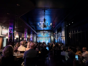 Audience members fill the dimly lit Hotel Congress Century Room as the Mohamed Abozekry Sextet performs on stage under warm spotlights. The jazz ensemble plays in front of a curtain backdrop, surrounded by chandeliers and atmospheric lighting.
