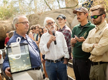 Several researchers and scientists gather around a glass container holding many small fish