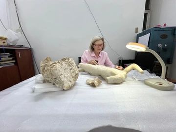 Irene Bald Romano sitting at a table in a lab with ancient marble sculptures under a lamp