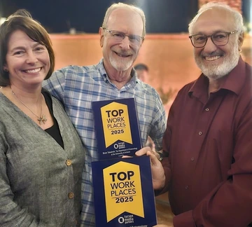 Three University of Arizona Department of Entomology leaders smile while holding two “Top Workplaces 2025” plaques. The awards are blue and yellow, and the group stands together at an indoor celebration event.