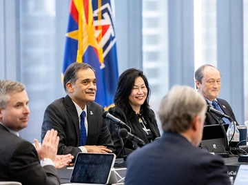 Several men and women take part in a discussion near the Arizona state flag and the University of Arizona flag