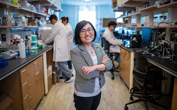 A woman stands in a lab near students doing research.