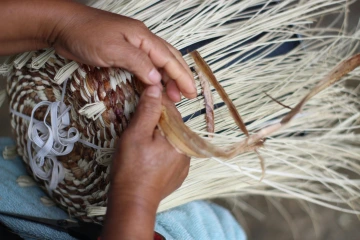 Close-up image of a woman weaving a traditional basket.