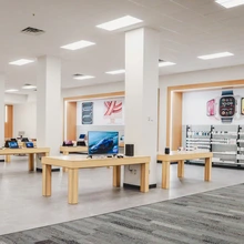 Interior the University of Arizona Campus Store featuring display tables with laptops, monitors and smartwatches. Shelves along the walls hold tech accessories, and signage reads "Technology Services." The space is brightly lit with white walls, wood accents, and a gray carpeted floor.