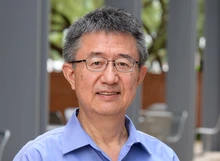 A man with glasses and a blue collared shirt stands near gray columns.