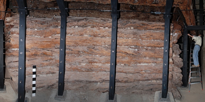 The stacked timbers form large, high walls, with a researcher standing on a step ladder to reach an upper plank