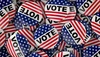 A pile of red, white, and blue "VOTE" buttons featuring stars and stripes, designed to resemble the American flag.