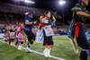 Hopi dancers performing a sacred corn dance in traditional tribal clothing on a football field with stadium lights shining down
