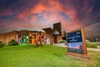 The exterior of the Flandrau Science Center and Planetarium at sunset. The building is constructed with red brick and features modern architectural designs, including a large dome that hints at its planetarium function. A series of rectangular windows are illuminated with various colors, creating a vibrant spectrum on the building's facade.
