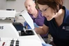 A man and a woman researcher analyze results over a white microscope.